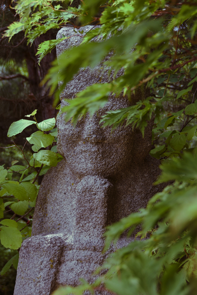 a stone Japanese statue is hidden behind foliage