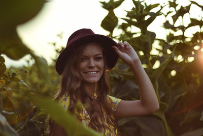 a young lady tilts her hat to hide her face from the setting sun in a corn field