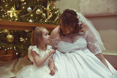 a blushing bride sits with her flower girl as she plays with the bride's veil